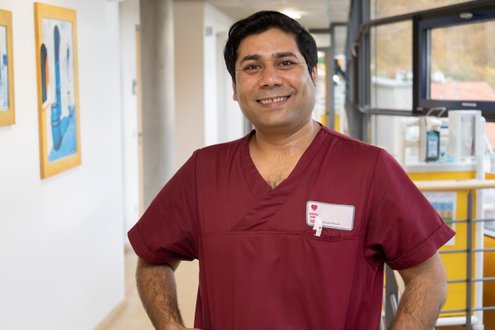 Pflegekraft in roter Uniform lächelt im Krankenhausflur.