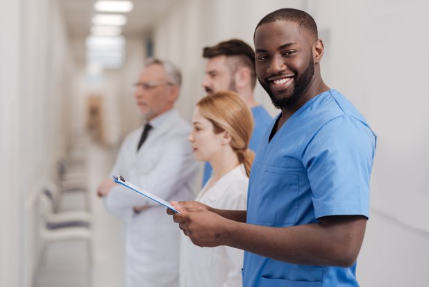 Lächelnder Arzt in blauer Uniform mit Klemmbrett im Krankenhausflur.