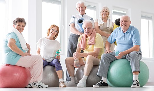 Seniorengruppe bei Gymnastikübungen auf Gymnastikbällen im Fitnessraum.