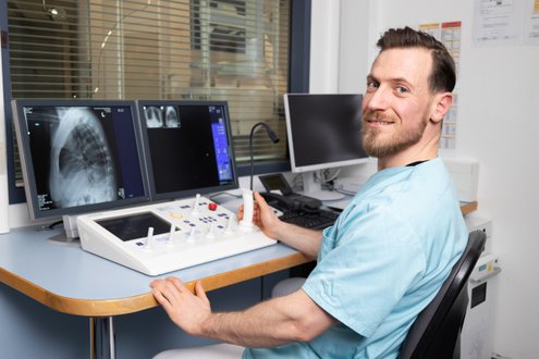 Techniker in Klinik überprüft Röntgenbilder auf Monitoren in Kontrollraum.