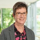 Porträt einer lächelnden Person mit Brille vor unscharfem Hintergrund.