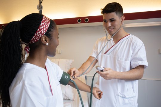 Zwei Pflegekräfte messen Blutdruck, Symbol für Menschlichkeit in der Pflege.