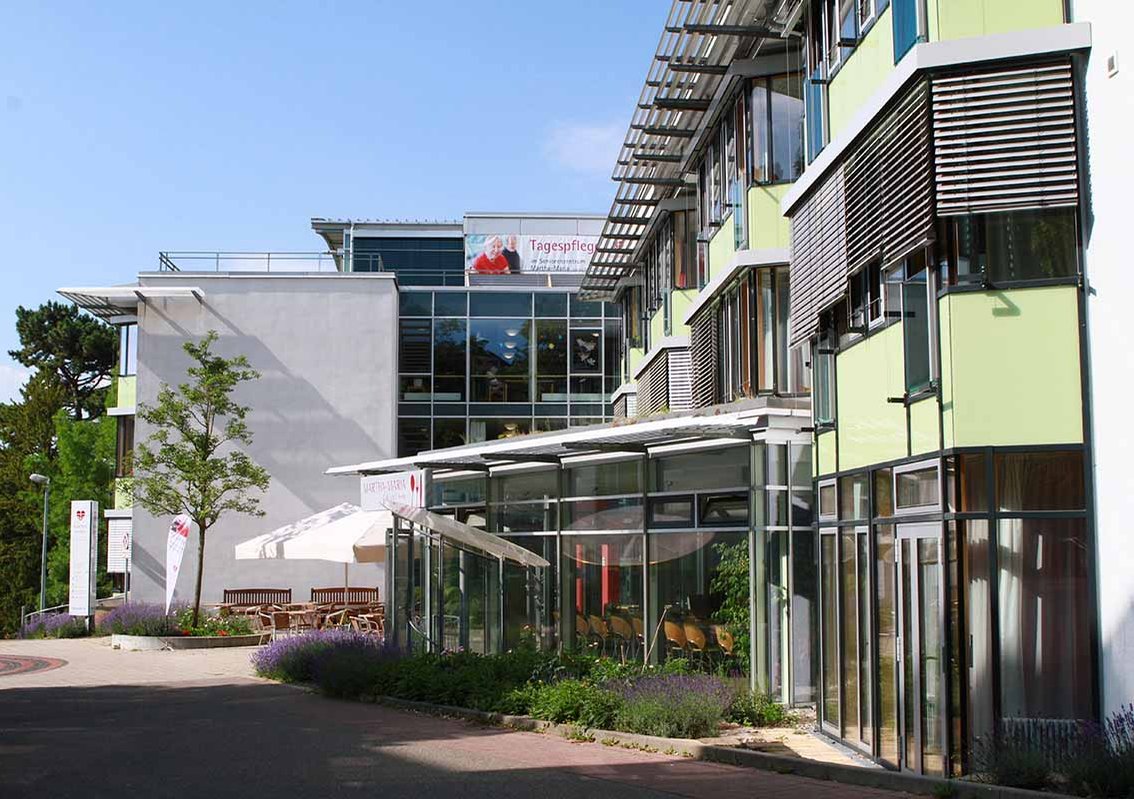 Modernes Gebäude mit grüner Fassade und Glasfront an einem sonnigen Tag.