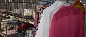 Garderobe mit bunten Hemden und gestapelter Kleidung in einem Regal.