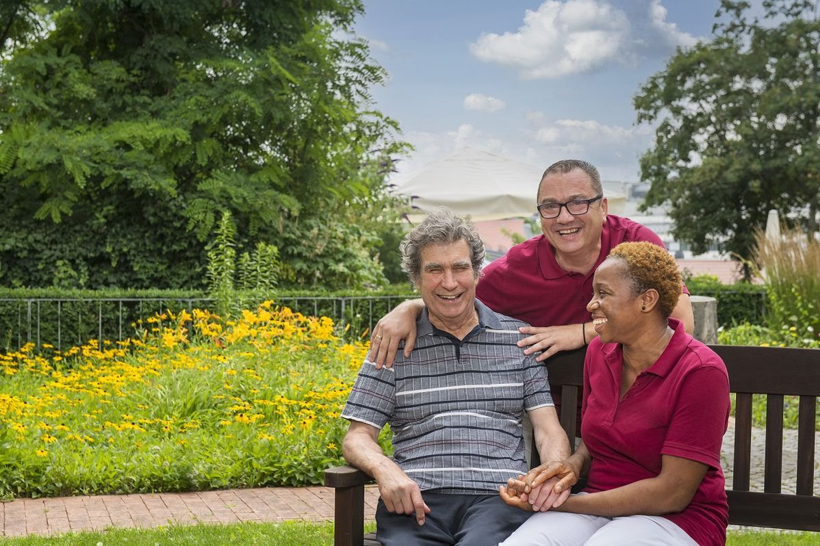 Drei Personen lächelnd auf einer Bank im Garten des Seniorenzentrums Stuttgart.