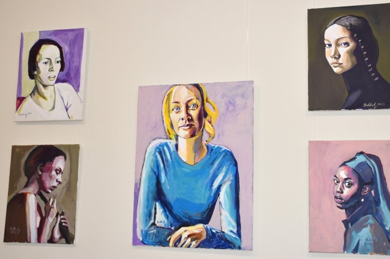 Fünf Porträtgemälde an einer weißen Wand ausgestellt.