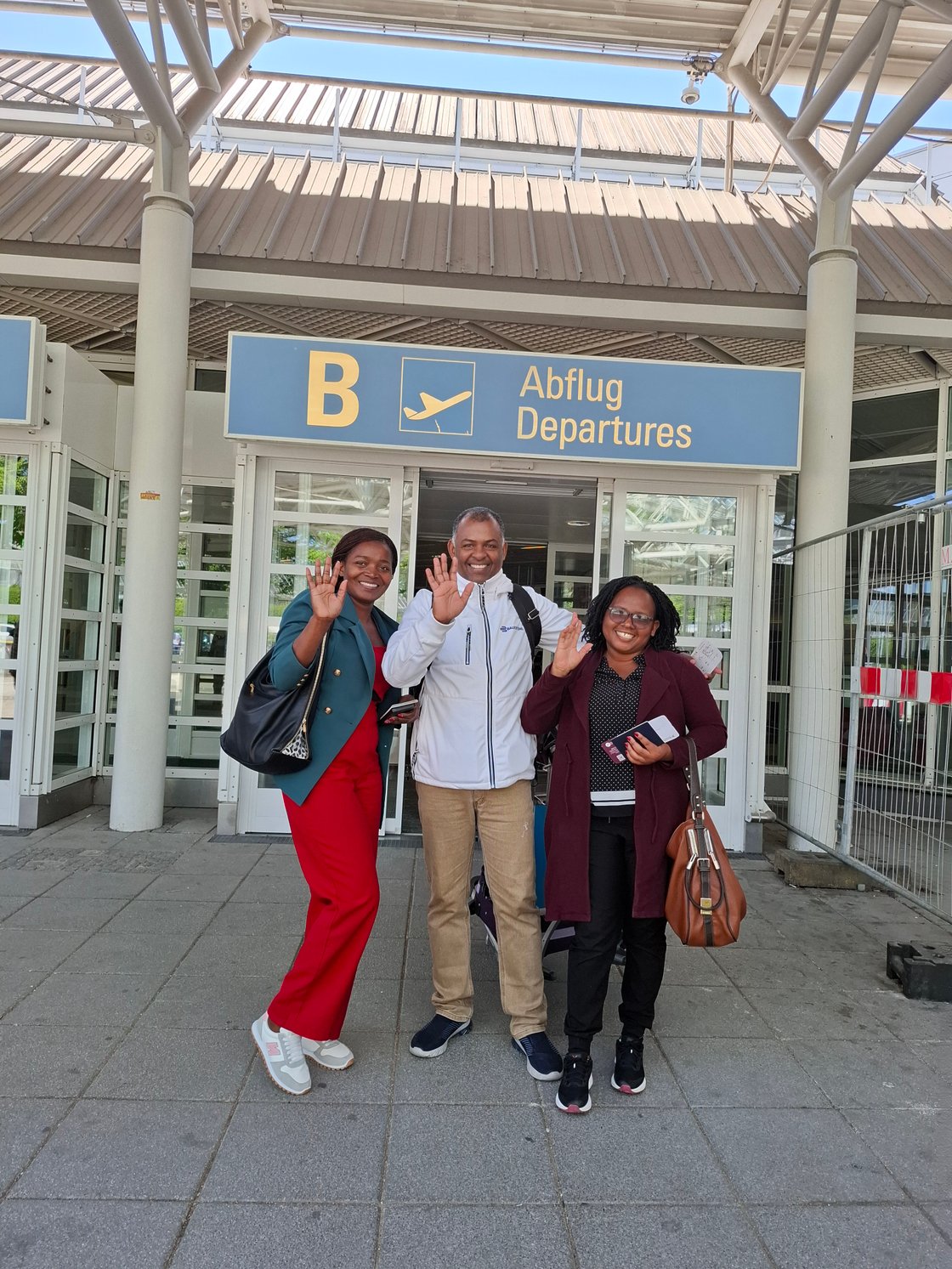 Drei Personen winken am Flughafen, Abflugbereich Mosambik.