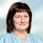 Porträt einer Frau in medizinischer Kleidung, lächelnd vor unscharfem Hintergrund.