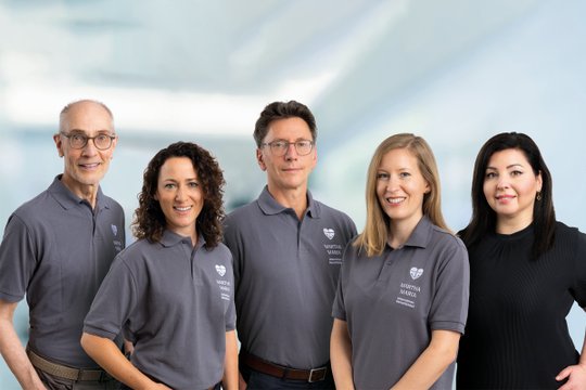 Fünf Personen in Martha-Maria-Poloshirts lächeln vor verschwommenem Hintergrund.