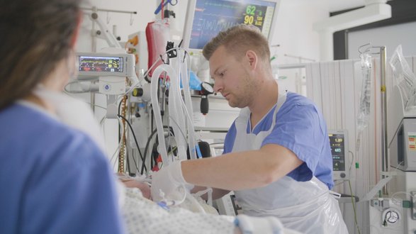 Krankenpfleger versorgt Patienten im Krankenhaus Martha-Maria, Intensivstation, medizinische Geräte sichtbar.