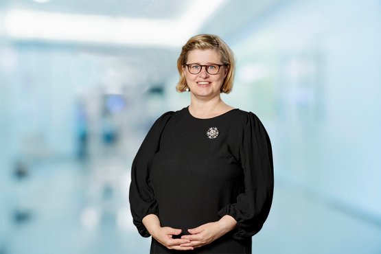 Frau in schwarzem Kleid vor unscharfem Krankenhausflur.