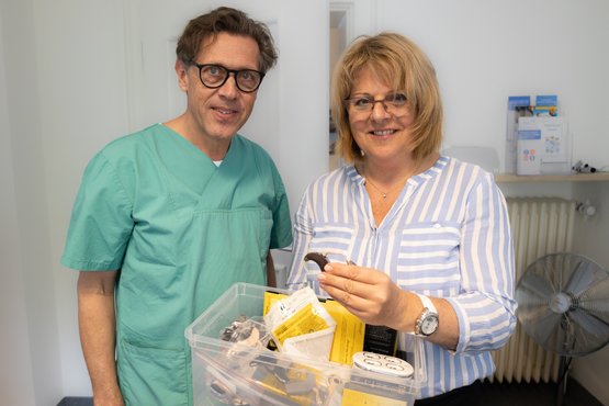 Zwei Personen präsentieren gesammelte Cochlea-Implantat-Teile in einer Kiste.