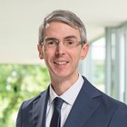 Mann im Anzug vor unscharfem, grünen Hintergrund lächelt freundlich.