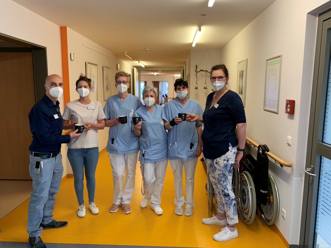 Pflegepersonal im Flur eines Pflegeheims mit Masken und Kaffeetassen.