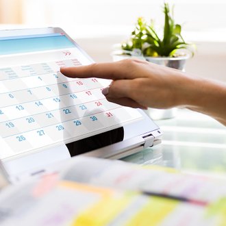 Finger tippt auf Tablet-Kalender, grünes Pflanze im Hintergrund.