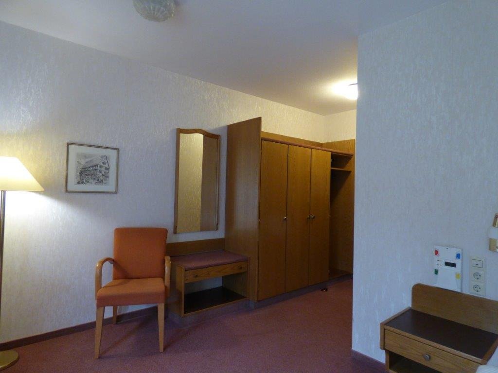 Krankenhauszimmer mit Sessel, Schrank und Lampe.