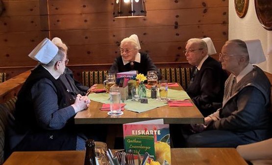 Vier Diakonissen sitzen in traditioneller Kleidung an einem Restauranttisch.