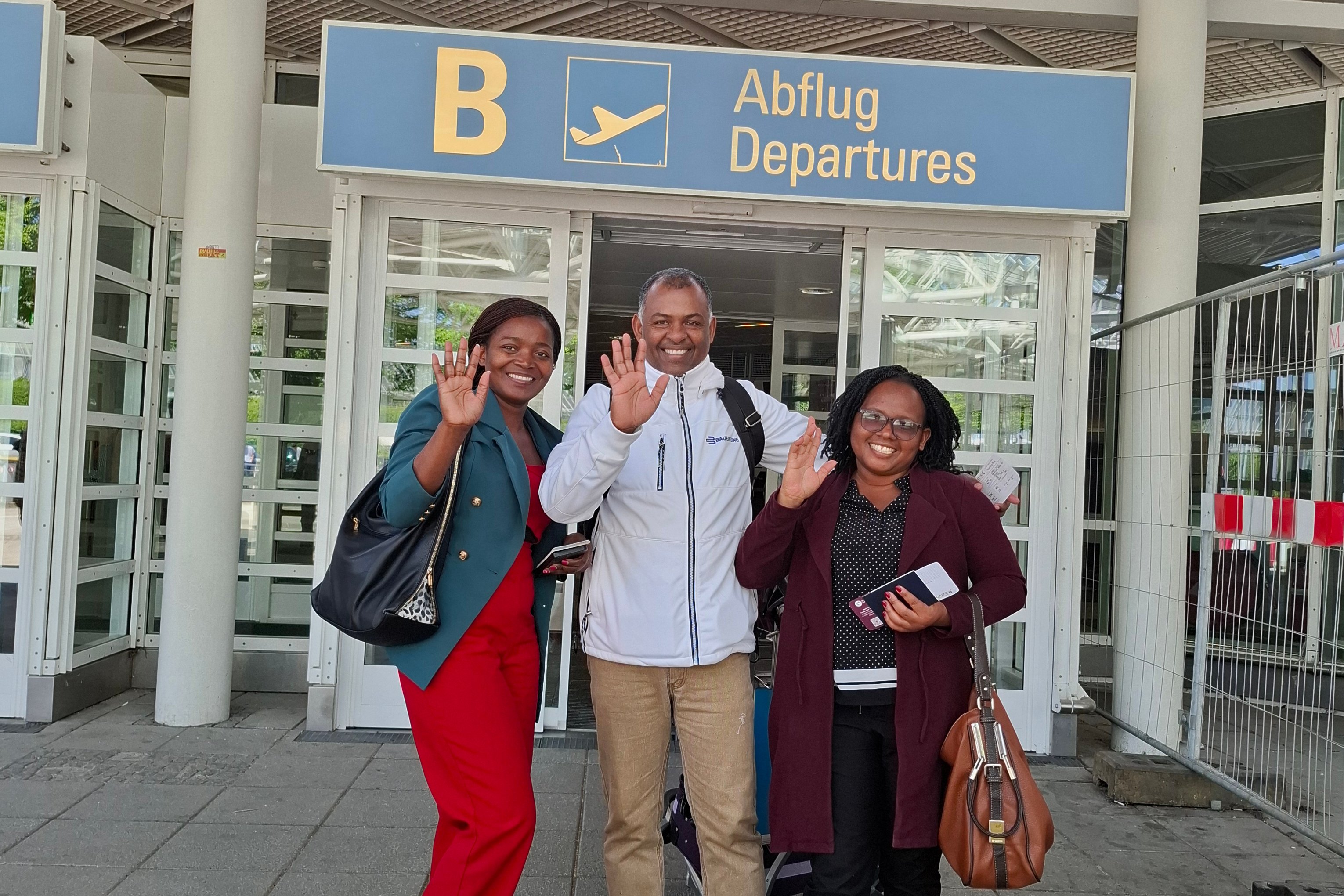 Drei Personen winken am Flughafen, Abflugbereich Mosambik.