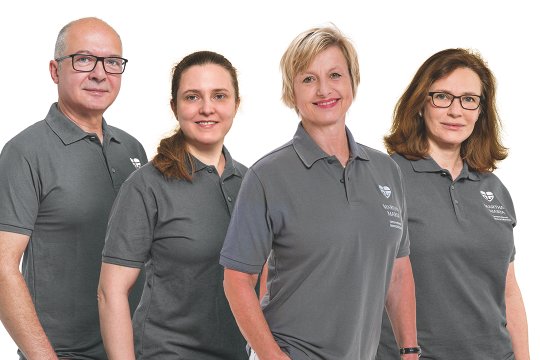 Vier Mitarbeitende in Martha-Maria-Poloshirts lächeln vor weißem Hintergrund.