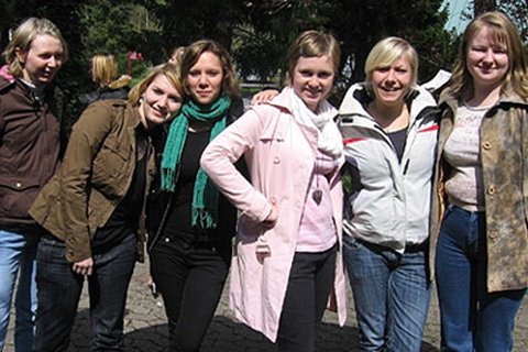 Sechs junge Frauen lächeln in die Kamera bei einem Seminar im Freien.