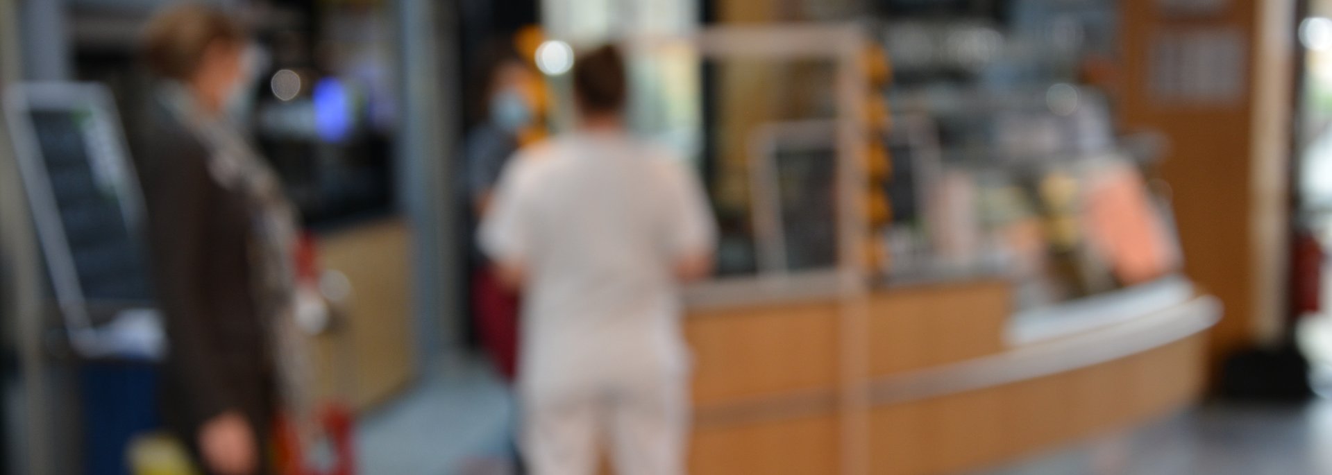 Verschwommene Szene im Krankenhaus-Bistro mit Menschen im Hintergrund.