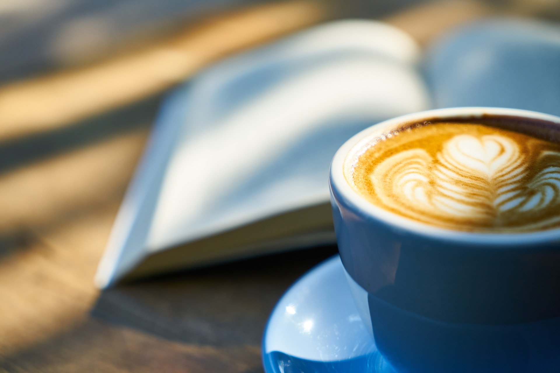 Nahaufnahme einer Tasse Kaffee mit Latte Art neben einem geöffneten Buch.