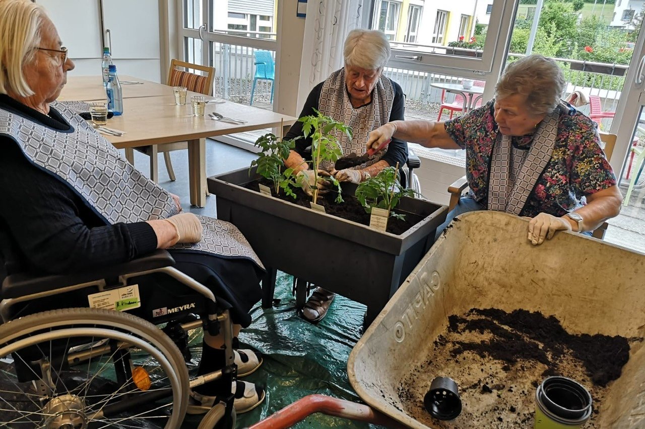 Drei ältere Frauen pflanzen gemeinsam in einem Raum im Seniorenzentrum.