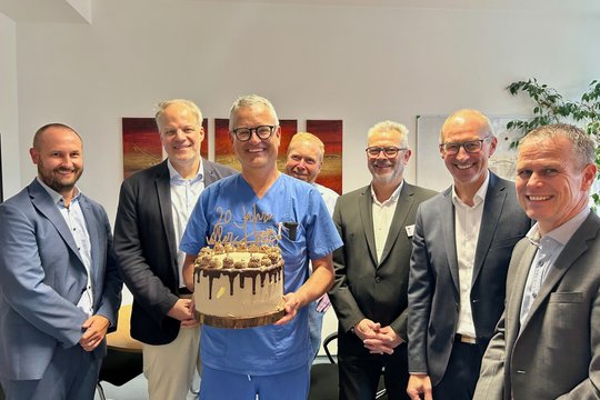 Mitarbeiter lächeln mit Jubiläumstorte im Krankenhaus.