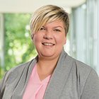 Porträt einer lächelnden Person in grauer Jacke vor unscharfem Hintergrund.