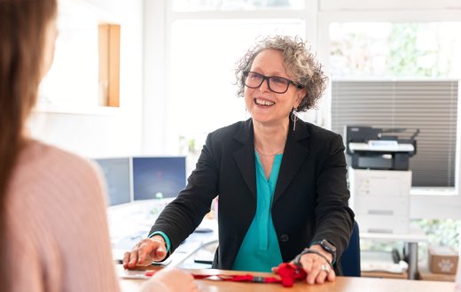 Frau am Empfangstresen lächelt, bereit zur Begrüßung eines Besuchers.