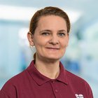 Porträt einer lächelnden Frau in rotem Polohemd vor unscharfem Hintergrund.