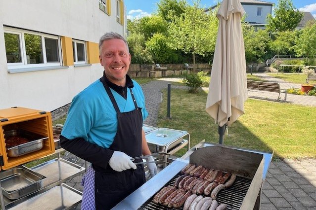 Mitarbeiter grillt Bratwürste im Garten des Seniorenzentrums Eckental.