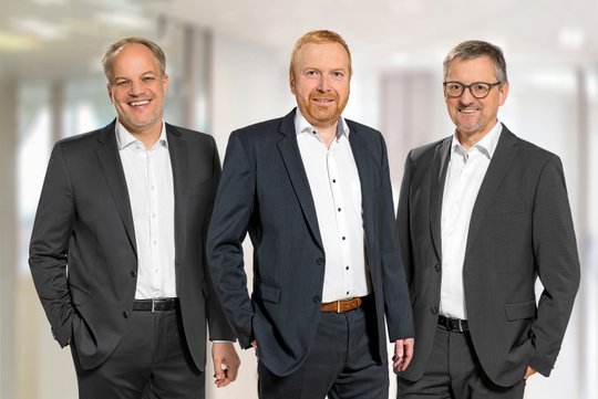 Drei Männer im Anzug, Vorstand des Diakoniewerks Martha-Maria, lächelnd vor hellem Hintergrund.