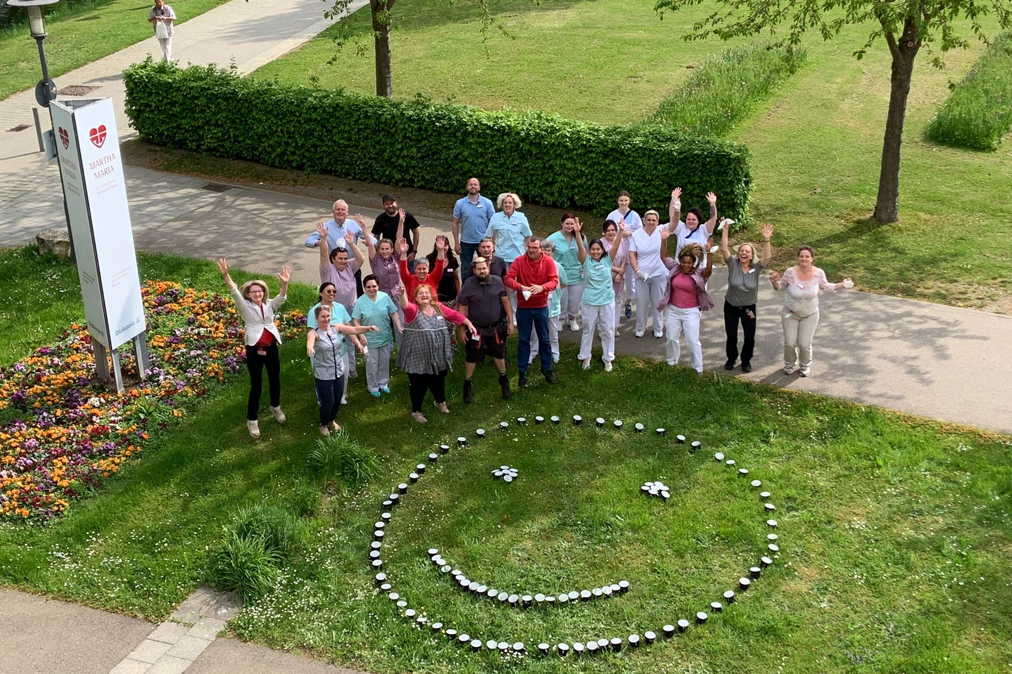 Gruppe von Menschen feiert lächelnd im Park neben einem Smiley aus Kerzen.
