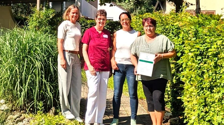 Vier Frauen stehen lächelnd im Garten, eine hält ein Zertifikat.