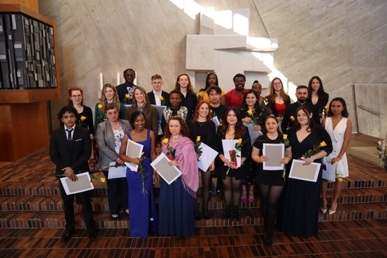 Gruppenfoto von Absolventen der Krankenpflegeschule mit Zertifikaten und Blumen.