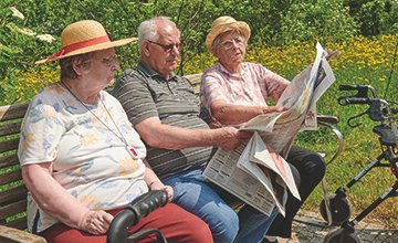 Drei Personen lesen eine Zeitung im Garten eines Martha-Maria-Seniorenzentrums.