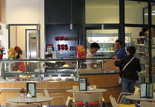 Krankenhaus-Bistro mit Gästen an der Theke und Tischen im Vordergrund.