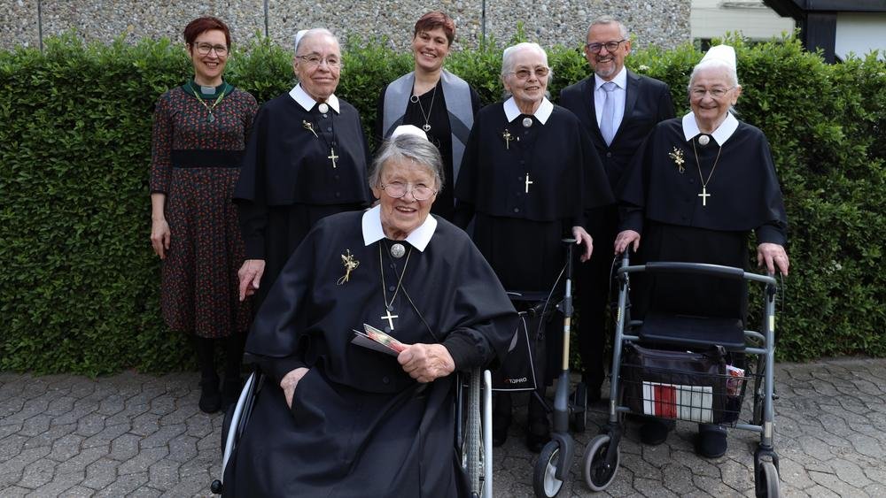 Sieben Personen, darunter Diakonissen in schwarz-weißer Kleidung, lächeln in die Kamera.