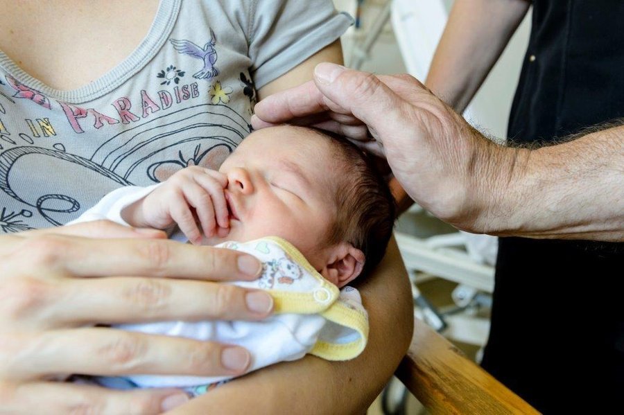 Baby im Arm der Mutter, wird liebevoll von einer Hand gesegnet.