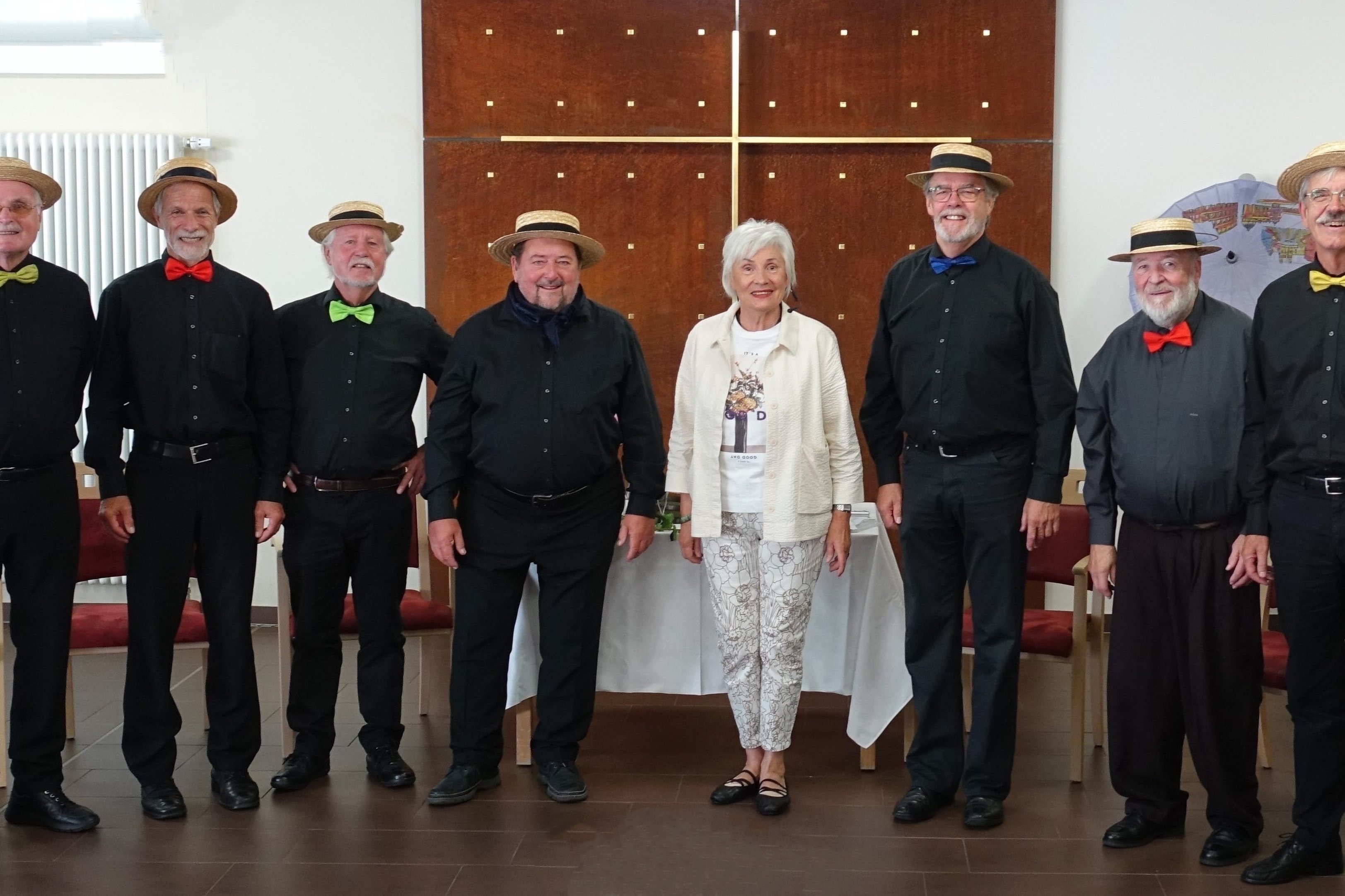Gruppe von älteren Menschen mit Strohhüten und Fliegen im Seniorenzentrum.