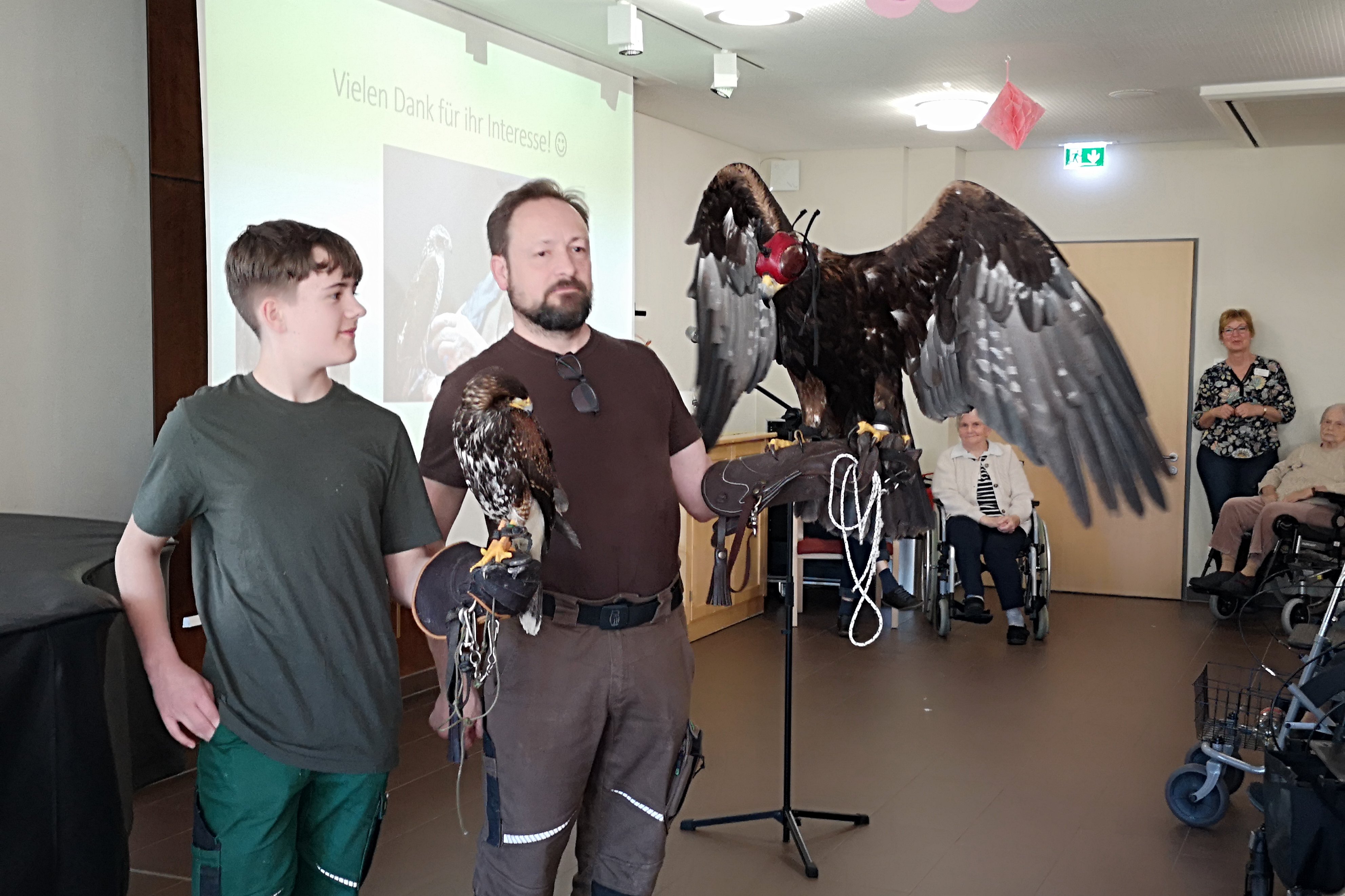 Falkner zeigt Greifvögel im Seniorenzentrum Eckental, Bewohner schauen zu.