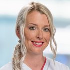 Lächelnde Krankenschwester in weißer Uniform vor unscharfem Hintergrund.