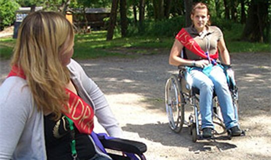 Zwei Personen im Rollstuhl im Freien bei einem Seminar.