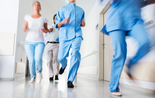 Ärzte in blauen Kitteln rennen eilig durch Krankenhausflur.