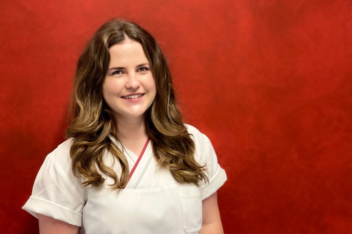 Frau in weißer Uniform vor rotem Hintergrund lächelnd porträtiert.