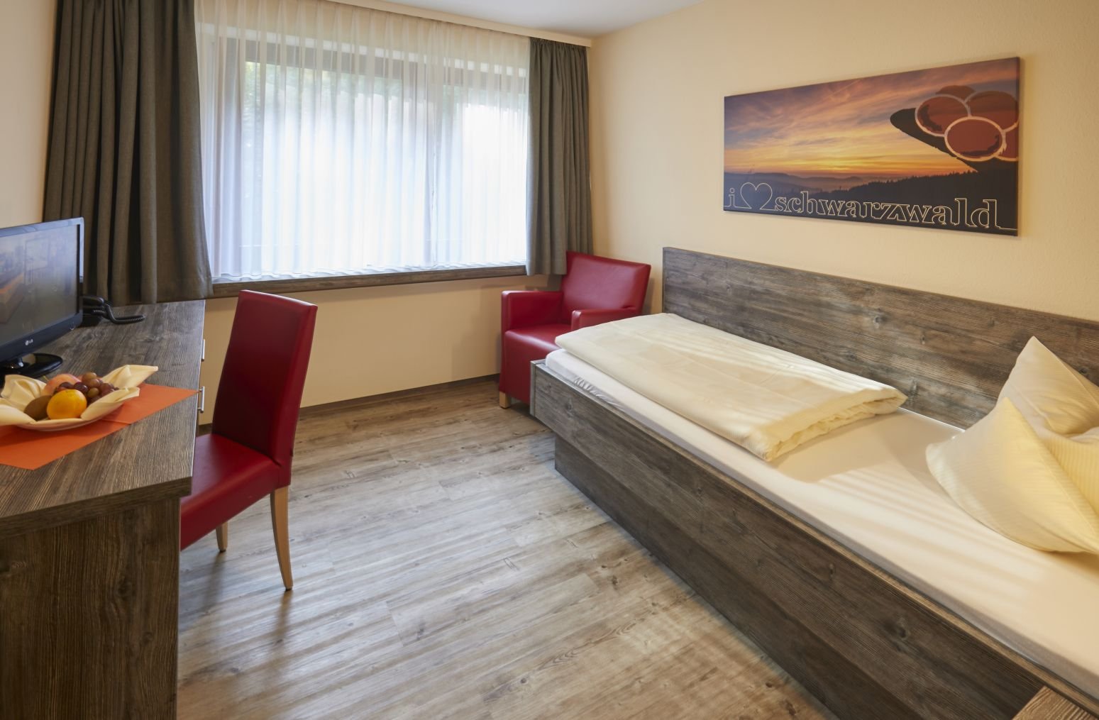 Komfortables Einzelzimmer mit TV, Schreibtisch und gemütlichem Sessel in Klinik.