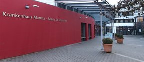 Eingang des Krankenhauses Martha-Maria St. Theresien mit roter Fassade.