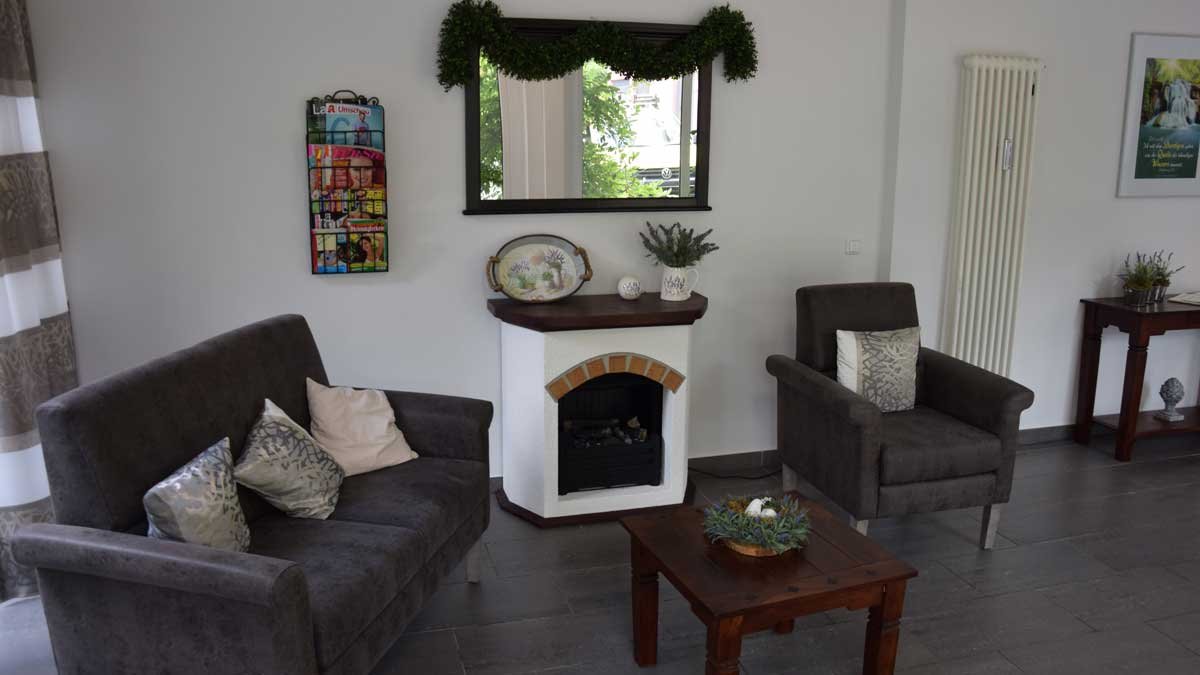 Gemütliches Wohnzimmer im Seniorenzentrum Nürnberg mit Kamin und grauen Sofas.
