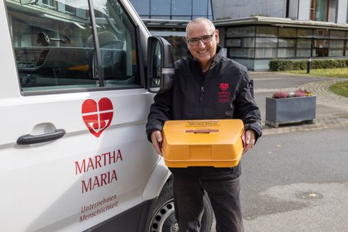 Mann mit Essensbox vor Martha Maria Fahrzeug, Seniorenzentrum.